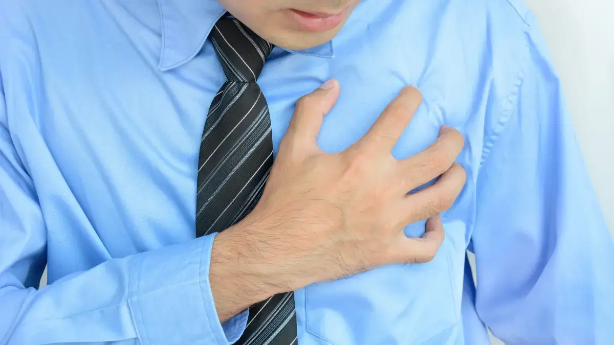Uomo in camicia e cravatta che si tiene il petto, simbolo di infarto da stress lavorativo